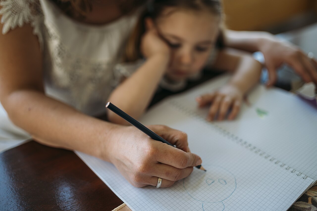 Un adulte accompagne un enfant qui dessine à une table